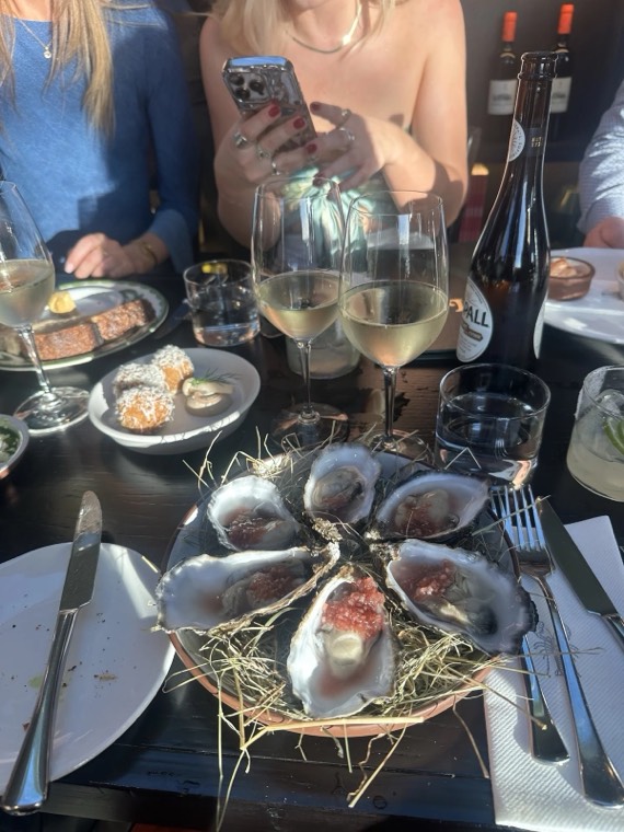 A table of oysters on straw with glasses of white wine