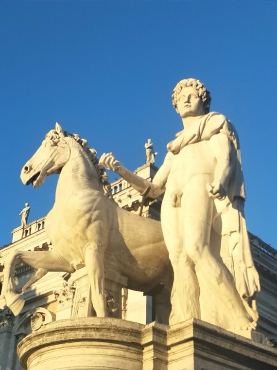 A statue of a horse and a standing figure against a blue sky in Rome