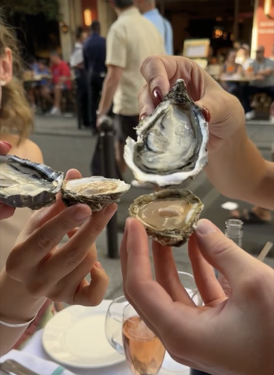 Guests holding open oyster shells at a sidewalk table in Paris