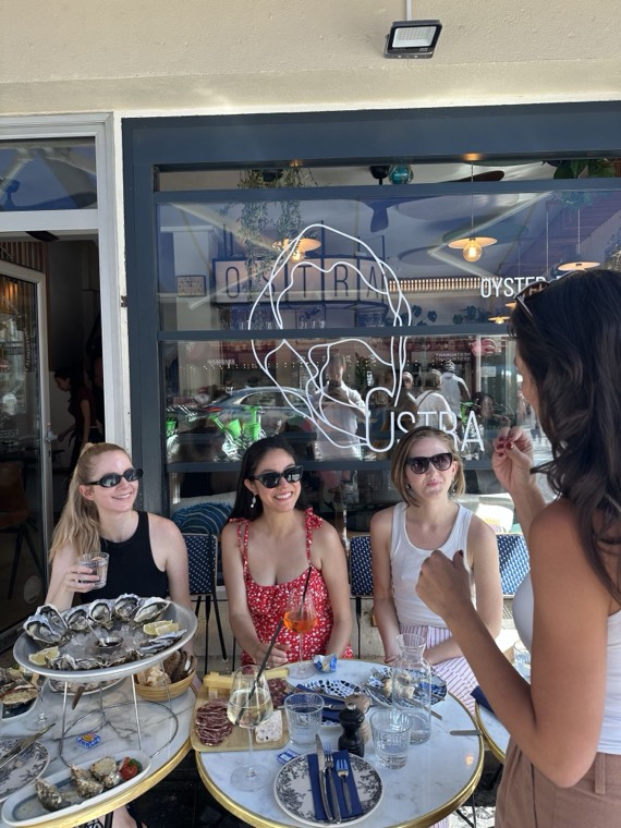 Guests seated outside Ostra oyster bar with a platter of oysters, while the guide talks to them