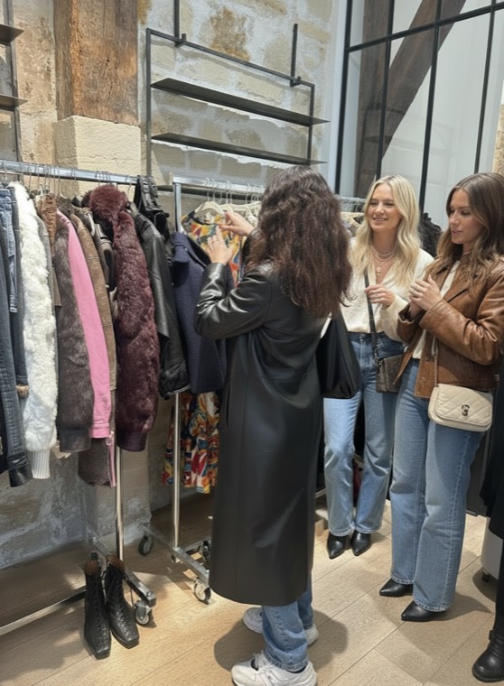 Guests browsing a rack of coats and jackets in a Paris vintage shop with stone walls and timber beams