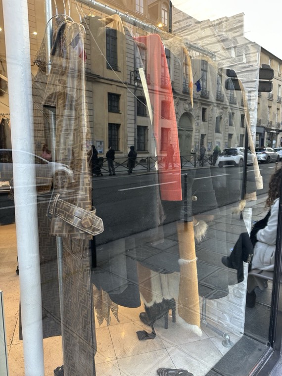 Coats on a rail seen through a vintage shop window, with a Paris street reflected in the glass