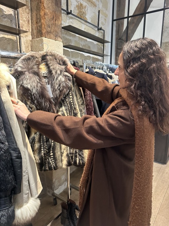 A guest examining a fur-collared coat on a rack in a Paris vintage boutique