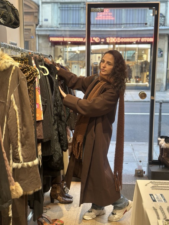 A guest browsing a rack of vintage coats and boots by the shop door