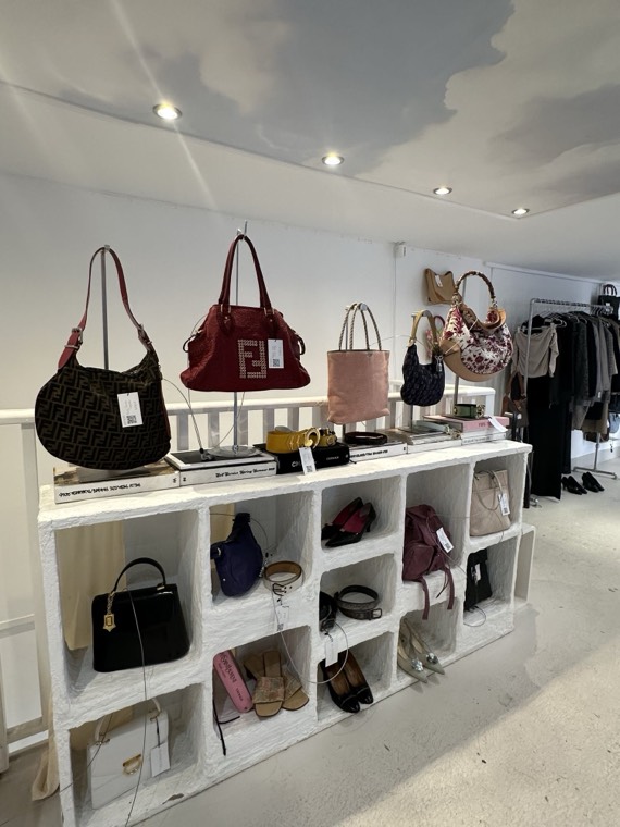 Designer handbags and shoes displayed on a white shelving unit in a vintage boutique